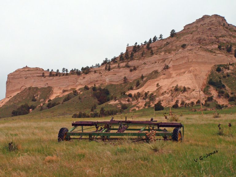 Platte River Basin Environments -old rusty farm equipment sitting in front of the bluffs by V G-Jones
